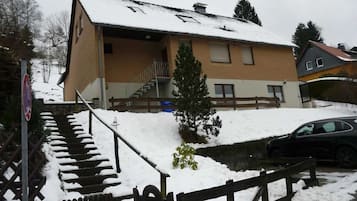 A two-story building with a sloped roof, a staircase leading to the entrance, and a small tree in front.
