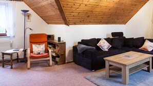 Una sala de estar acogedora con techo de madera, un sofá negro, una mesa de centro de madera y un sillón con cojín.