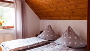 Una habitación con dos camas, almohadas con estampado de estrellas, una ventana con cortinas y techo de madera.