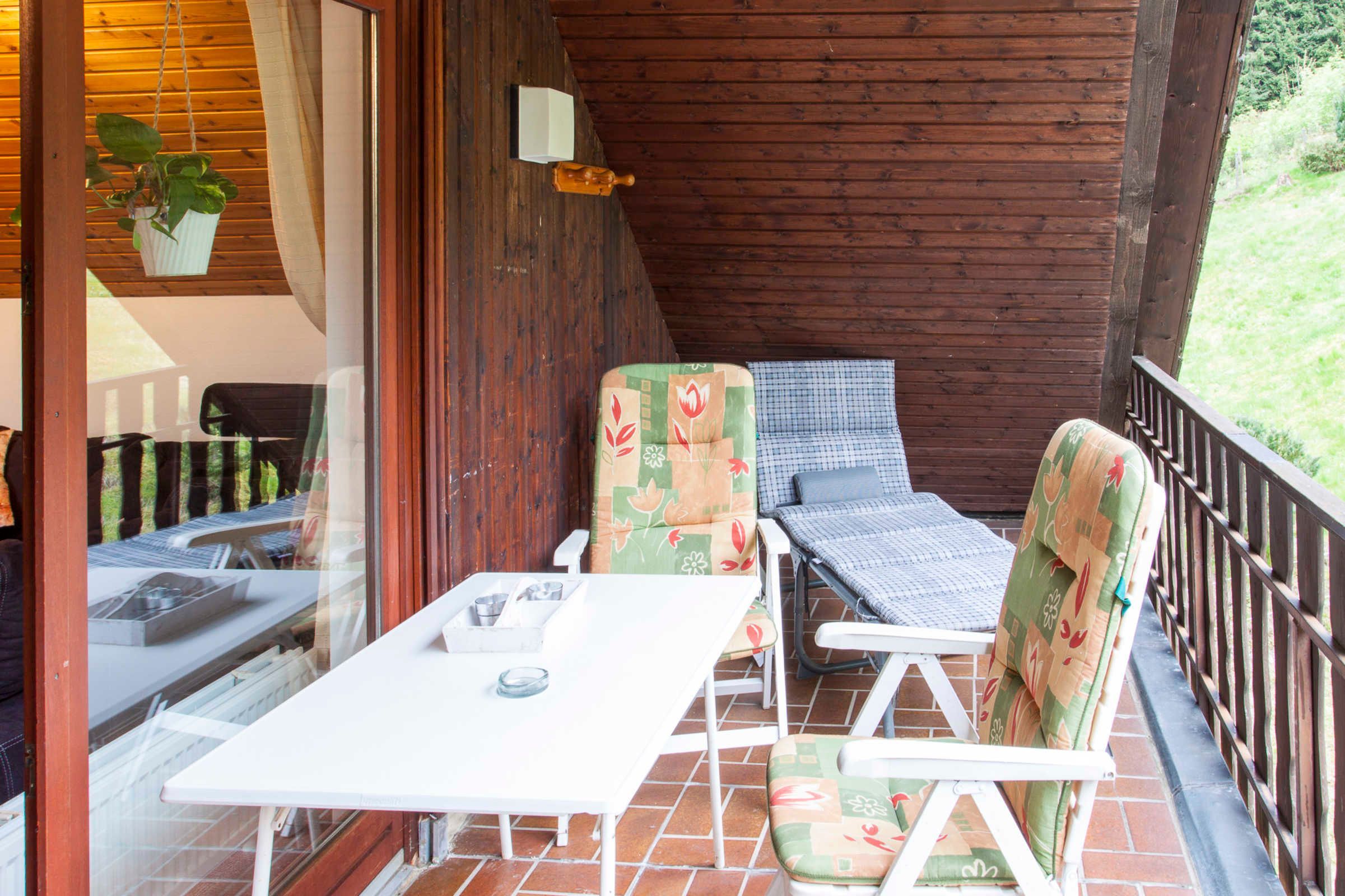 A covered outdoor seating area with a table and chairs, a hanging plant, and a view of the outdoors.