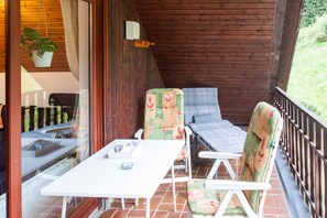 Ein überdachter Außenbereich mit Tisch und Stühlen, einer hängenden Pflanze und Blick ins Freie.