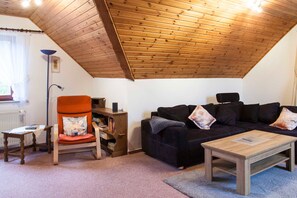 Ein gemütliches Wohnzimmer mit Holzboden, einer schwarzen Couch, einem Holztisch und einem Sessel mit Kissen.