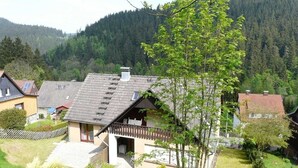 Una casa con techo inclinado, un balcón y un jardín con un árbol.