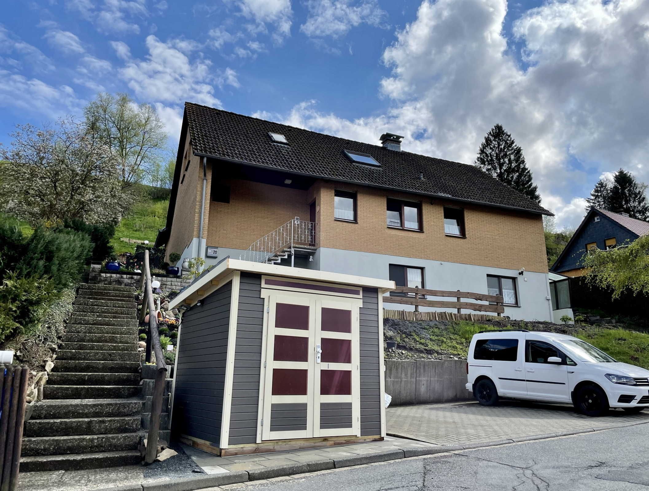 Ein zweistöckiges Haus mit kleiner Garage, einer Treppe zum Eingang und einem geparkten weißen Auto.
