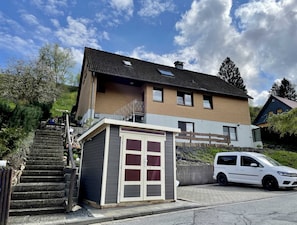 Ein zweistöckiges Haus mit kleiner Garage, einer Treppe zum Eingang und einem geparkten weißen Auto.