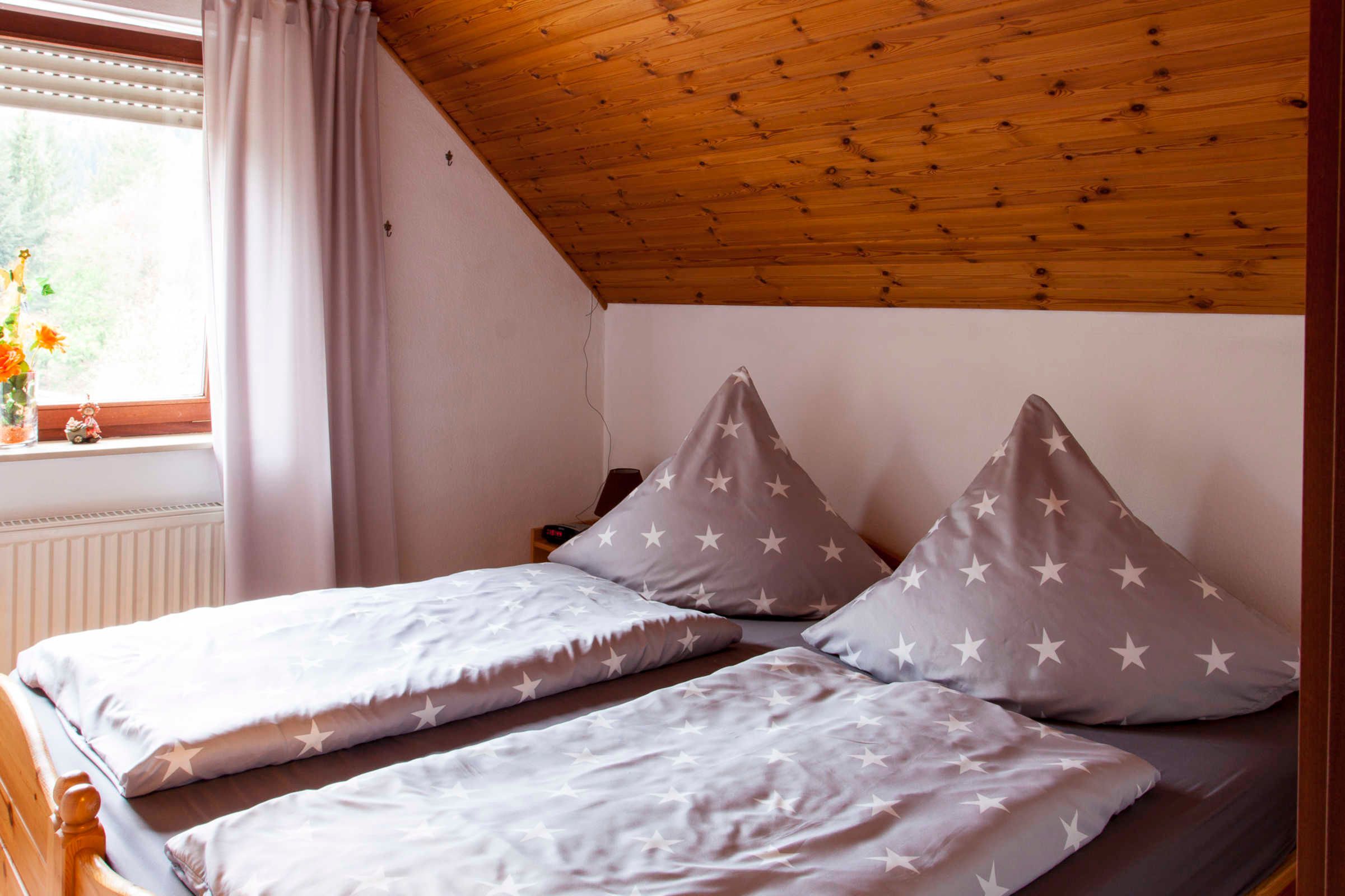Une chambre avec deux lits, des oreillers à motifs étoilés, une fenêtre avec des rideaux et un plafond en bois.