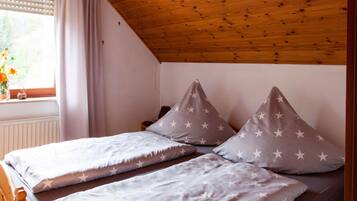 Une chambre avec deux lits, des oreillers à motifs étoilés, une fenêtre avec des rideaux et un plafond en bois.