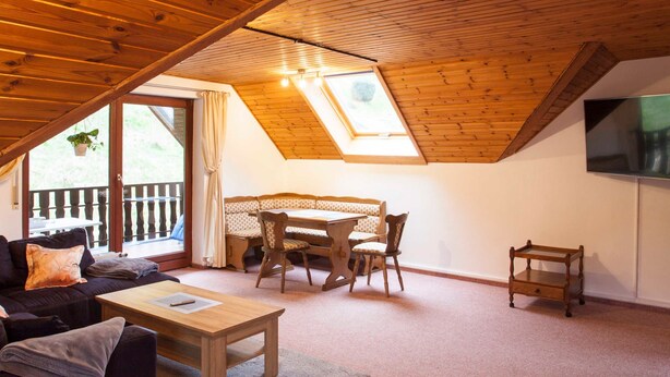 Una habitación acogedora con techo de madera, una mesa de comedor con sillas, un sofá y una pequeña mesa de madera.