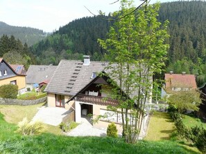 Ein Haus mit geneigtem Dach, einem Balkon und einem Garten mit Baum.