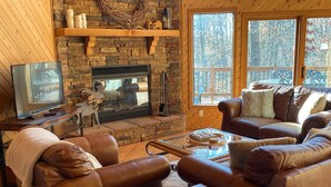 Ein gemütliches Wohnzimmer mit Kamin aus Stein, Ledersofas, einem Couchtisch und einem Fernseher.