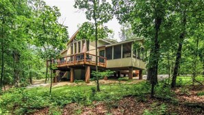 Eine zweigeschossige Holzdiele mit Terrasse, umgeben von dichtem Wald.