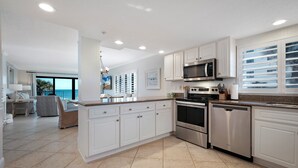 A modern kitchen with white cabinets, stainless steel appliances, and a large island. - Direct oceanfront 2/2 corner condo with large wrap-around balcony and heated pool (New Smyrna Beach)