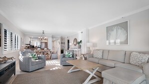 A spacious living room with a sofa, armchairs, and a coffee table. There is a dining area in the background with a table and chairs. - Direct oceanfront 2/2 corner condo with large wrap-around balcony and heated pool (New Smyrna Beach)