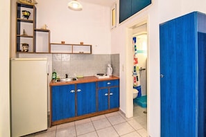 Uma cozinha compacta com geladeira branca, armários azuis e painel atrás do fogão em azulejos.