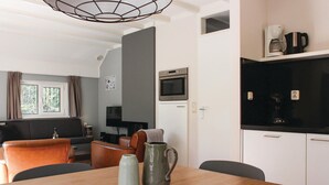 A modern kitchen with a microwave, coffee maker, and kettle. There is a dining table with chairs and a vase.