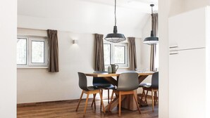 A dining area with a wooden table and chairs, two pendant lights, and a window with curtains.