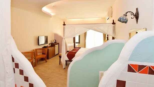 Un dormitorio con cama con dosel, un escritorio con silla, un televisor y una mesita de noche.