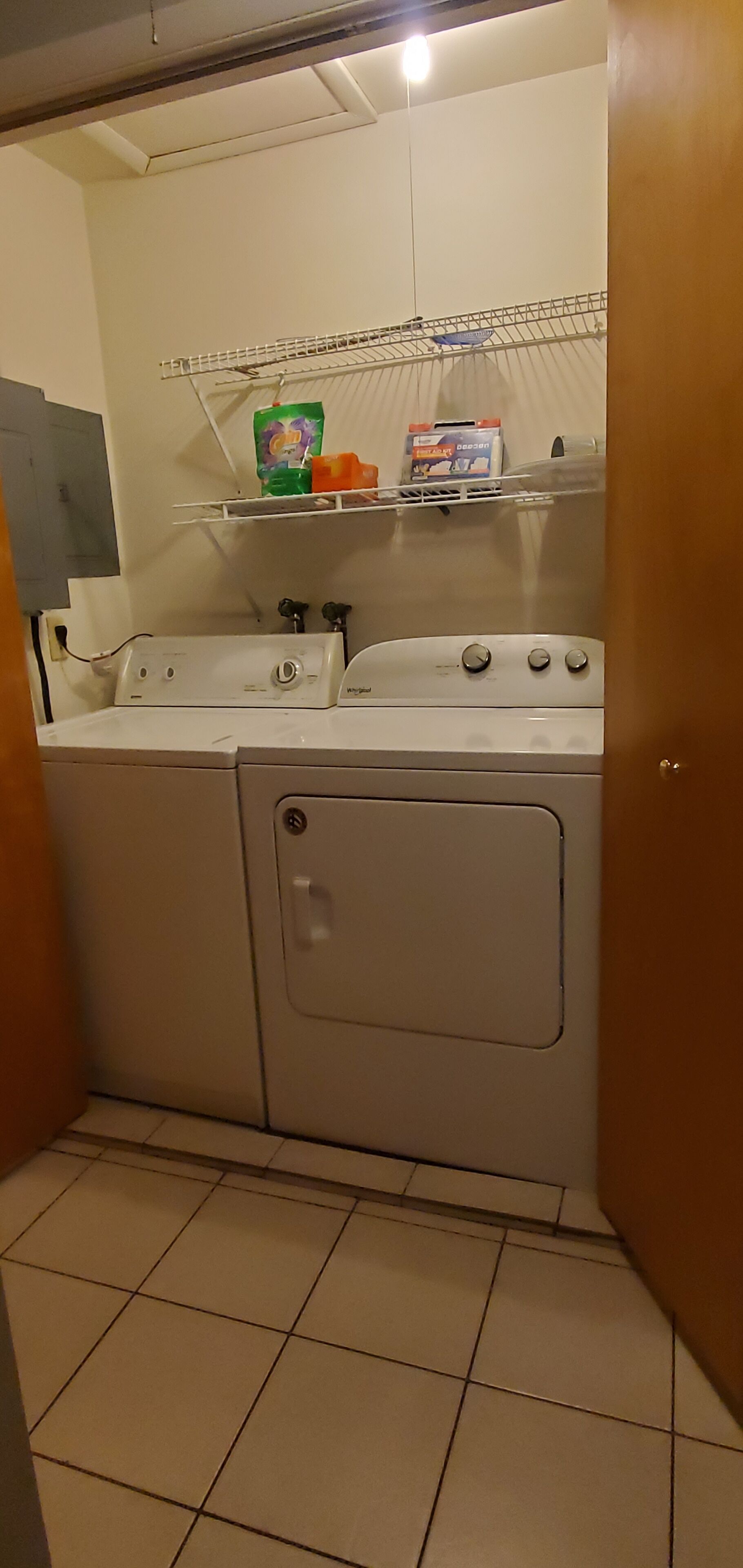 Een wasruimte met een wasmachine, droger en boven gelegen planken met schoonmaakmiddelen.