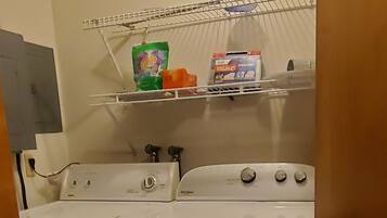 Een wasruimte met een wasmachine, droger en boven gelegen planken met schoonmaakmiddelen.