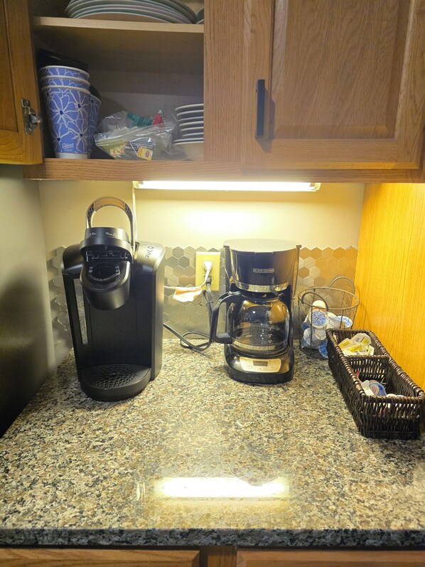 A kitchen with a coffee maker, a kettle, and a basket on the counter.