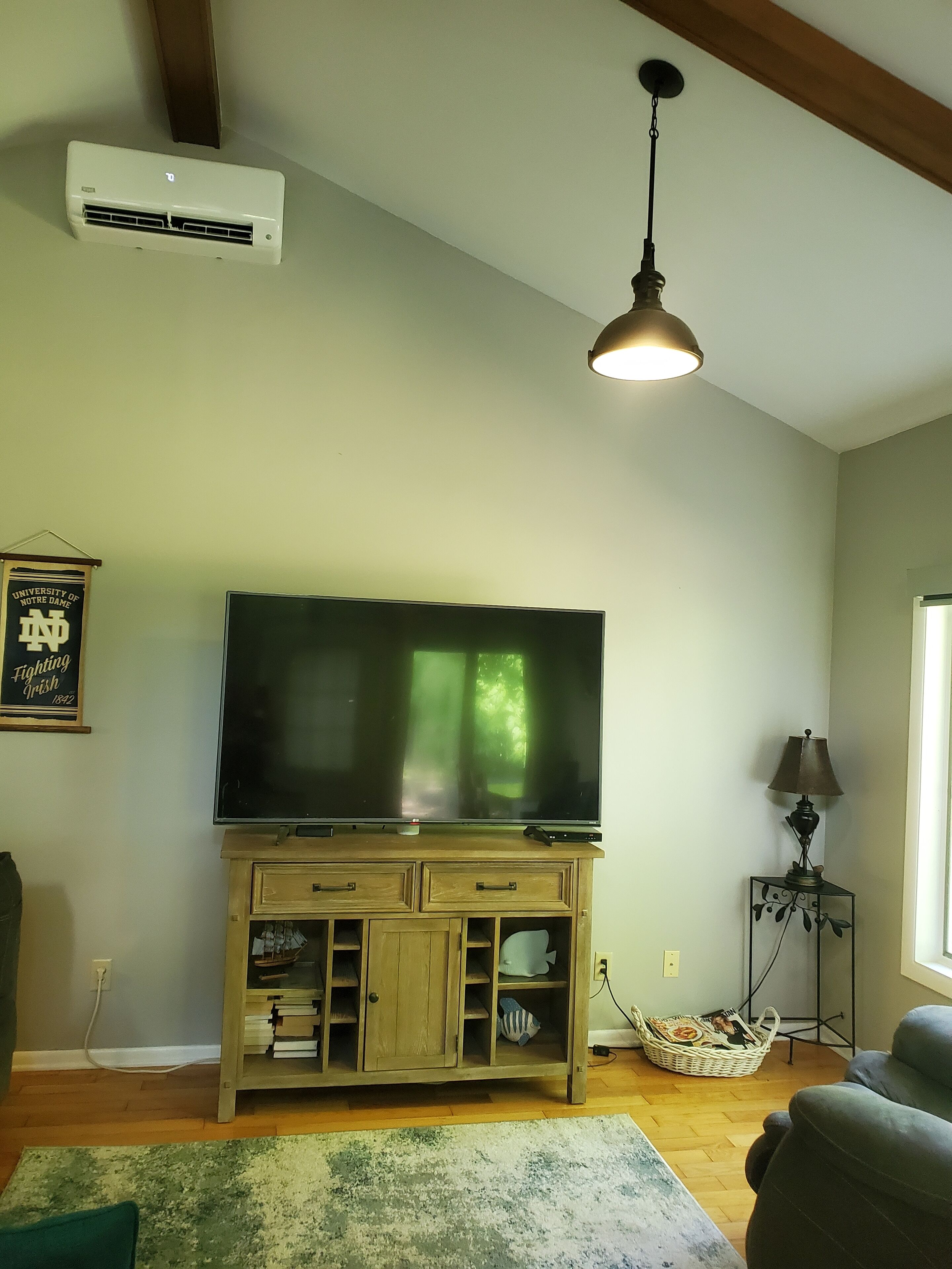 Un salon avec un téléviseur à écran plat posé sur un meuble en bois, un ventilateur de plafond, une lampe et une fenêtre laissant entrer la lumière naturelle.