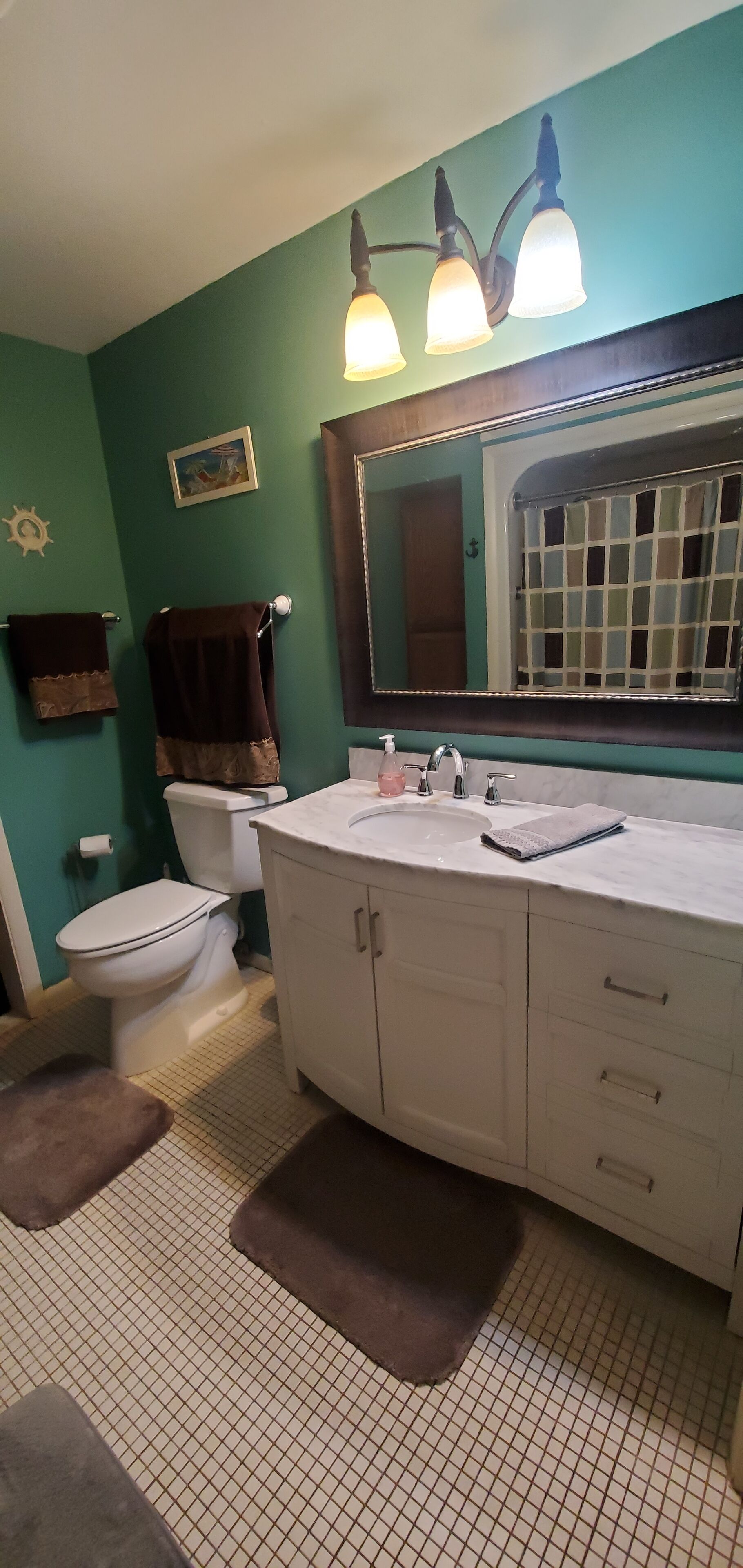 A bathroom with a white sink, a mirror, and a toilet. There are two towels hanging on the wall, and a rug on the floor.