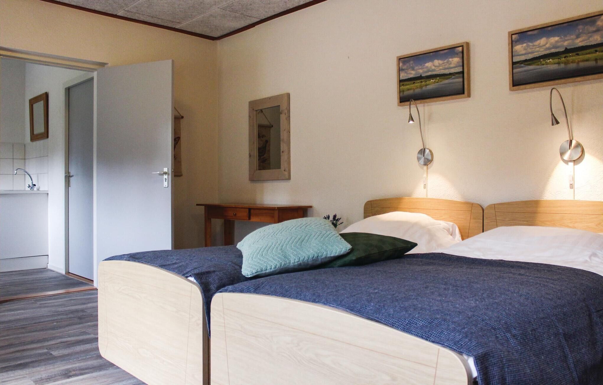 A room with two beds, a small table, a mirror, and two framed pictures on the wall.