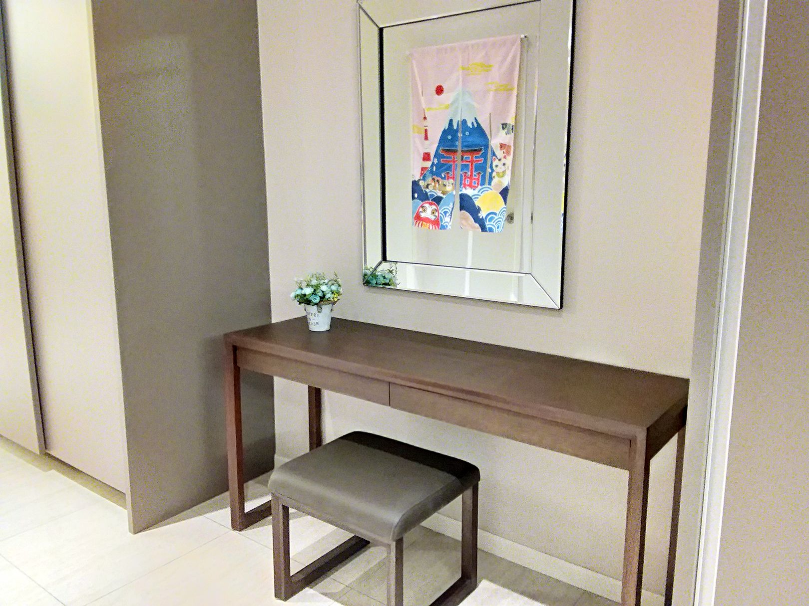 Una habitación con una consola de madera, un banco, una planta pequeña en maceta y un cuadro en la pared.