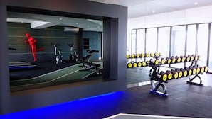 Un gimnasio moderno con equipamiento de ejercicio, un espejo grande y un estante con mancuernas.