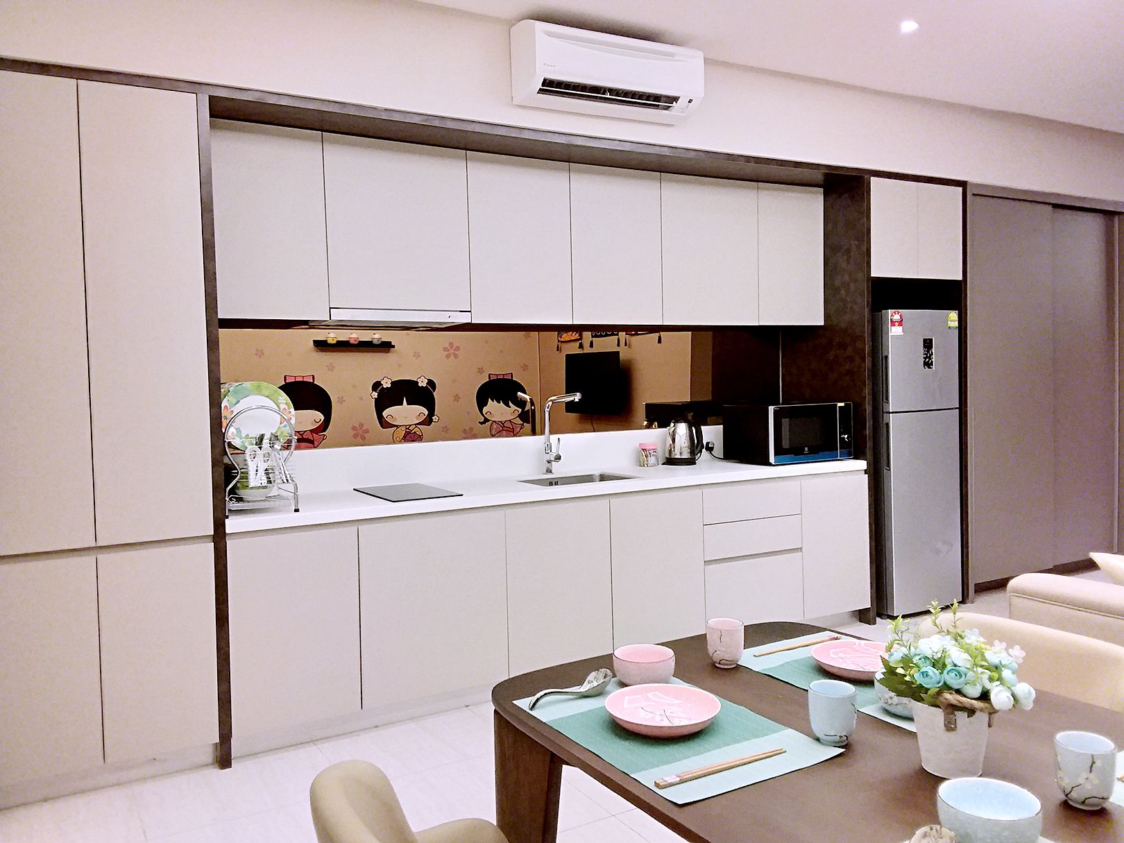 A modern kitchen with white cabinets, a microwave, a refrigerator, and a dining table set with pink plates and chopsticks.