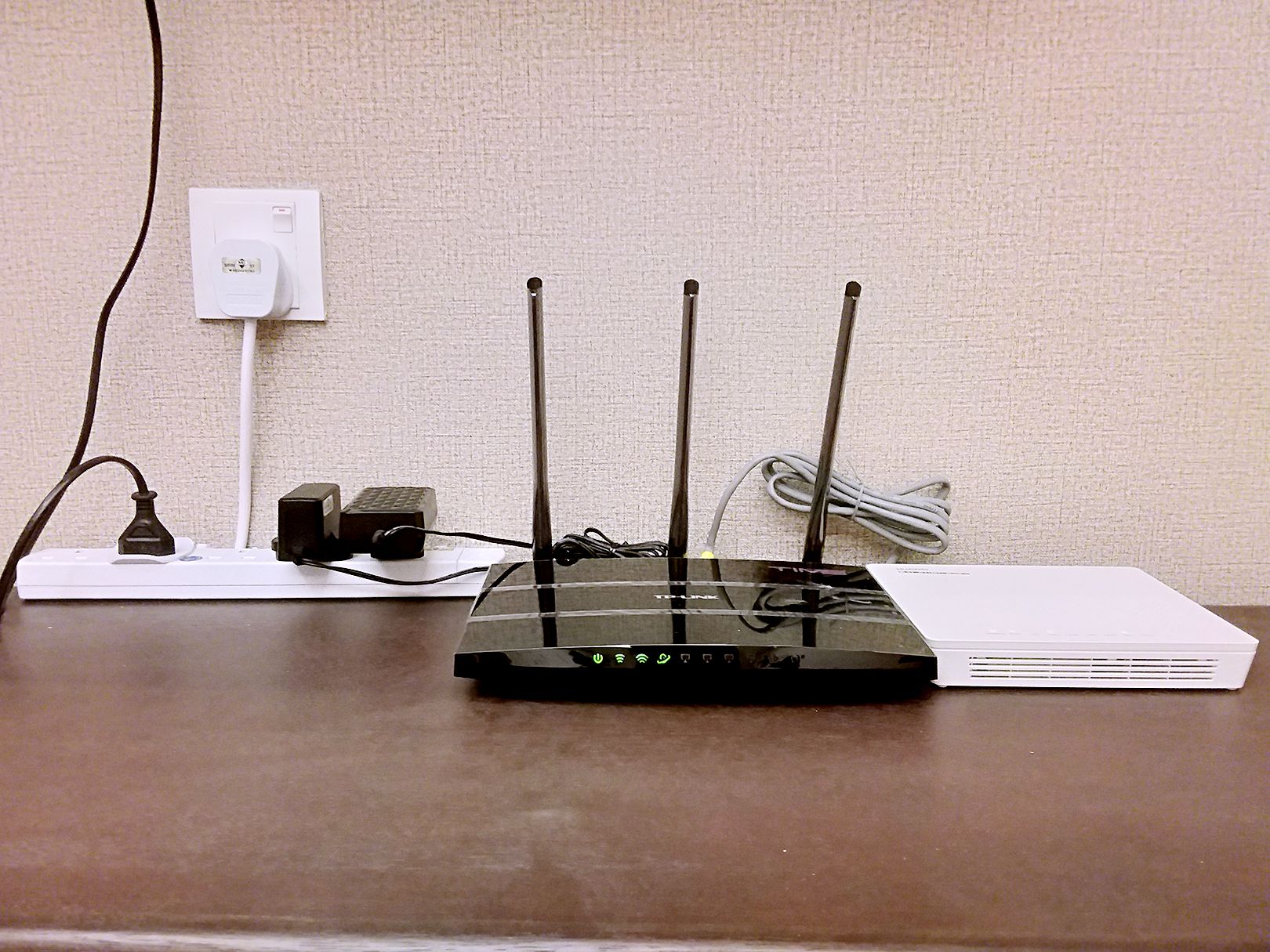 Un routeur doté de quatre antennes, posé sur un bureau, et branché à une multiprise et à une prise murale.