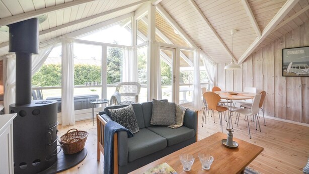 A cozy room with a large window, a sofa, a table, and a wood-burning stove. - 2 bedroom stunning home in Væggerløse (Væggerløse)