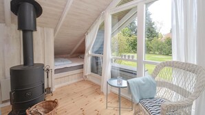 A cozy attic bedroom with a wood-burning stove, a wicker chair, and a view of the garden. - 2 bedroom stunning home in Væggerløse (Væggerløse)