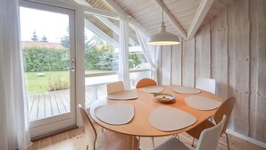 A round wooden table with six chairs, a hanging light fixture, and a view of a garden through a glass door. - 2 bedroom stunning home in Væggerløse (Væggerløse)
