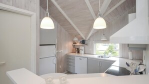 A modern kitchen with white cabinetry, a built-in dishwasher, a coffee maker, and pendant lighting. - 2 bedroom stunning home in Væggerløse (Væggerløse)