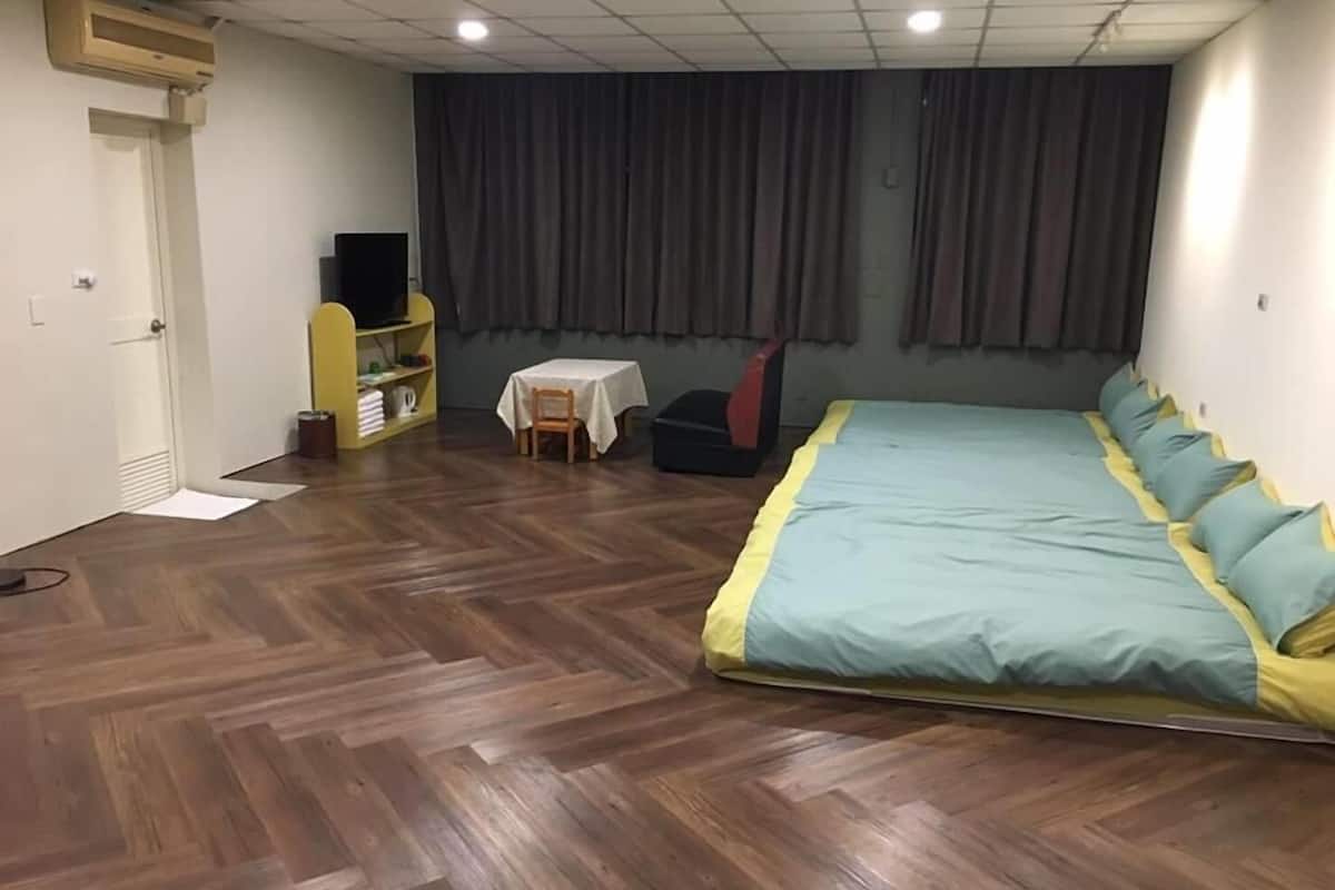 A room with a large bed, a small table with a chair, a television on a stand, and a wardrobe.