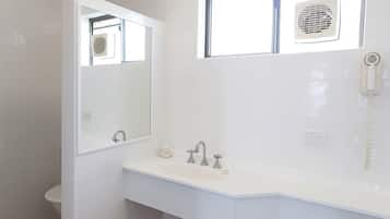 A modern bathroom with a white sink, two faucets, a mirror, a window with a fan, and a hairdryer.