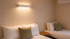 A hotel room with two beds, a round wooden side table, and a brick wall. - Busselton Motel (West Busselton)