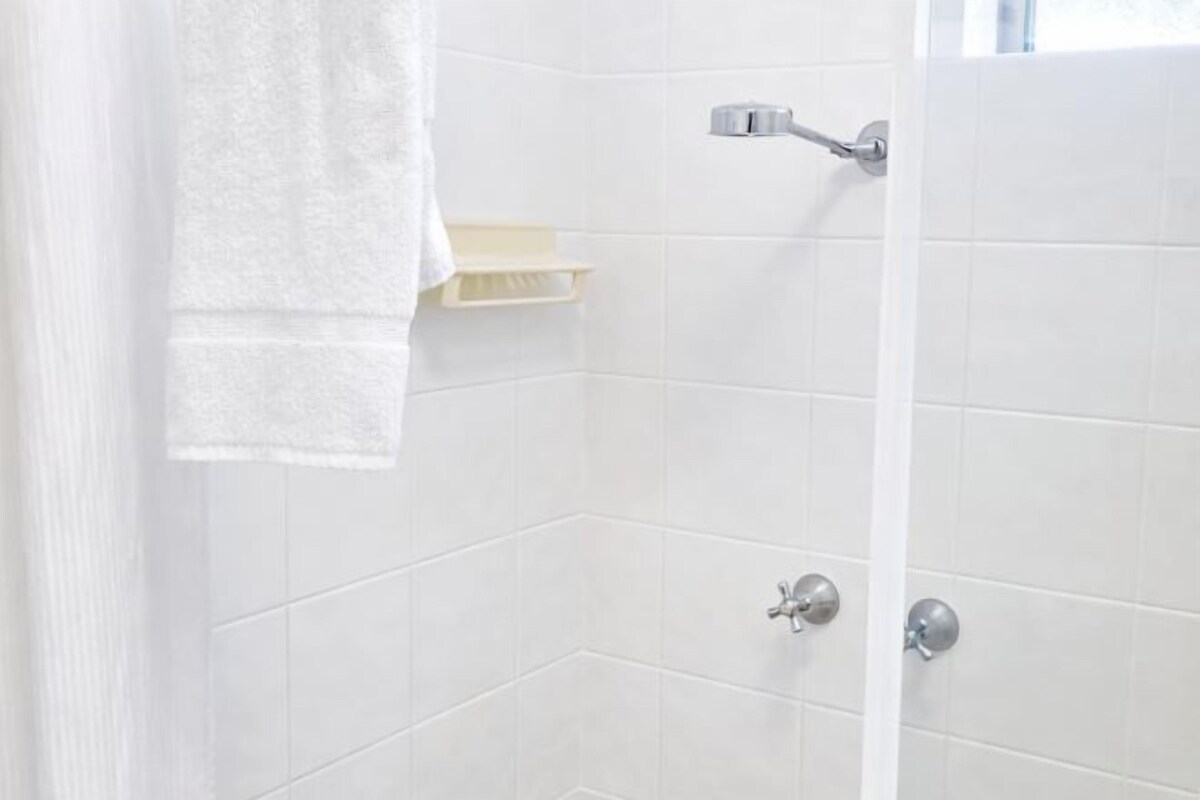 A shower with white tiles, a towel hanging on the wall, and a shelf with toiletries.