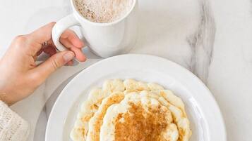 A white marble surface with a white plate of pancakes and a white cup of coffee.