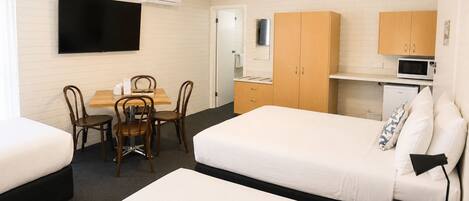 A hotel room with two beds, a dining table with chairs, a TV, a microwave, and a refrigerator.