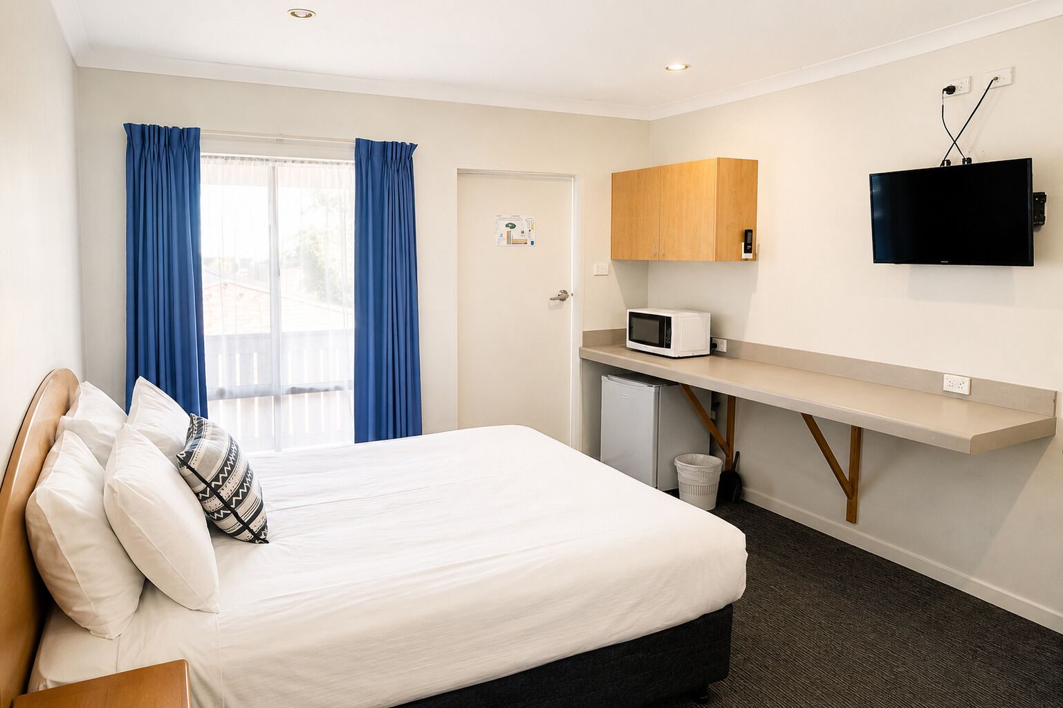 Une chambre d’hôtel comprenant un lit, un bureau avec un micro-ondes, une télévision et une porte donnant sur un balcon.