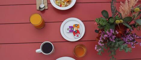 A breakfast setting with a plate of pancakes, a bowl of cereal with fruits, a glass of orange juice, a cup of coffee, a glass of tea, and a small plate with three packets of ZOOSH.
