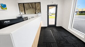 A reception desk with a computer, a clock, and a door leading outside. - Busselton Motel (West Busselton)