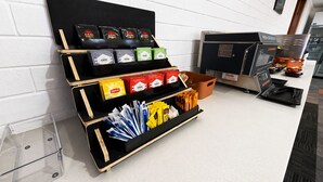 A hotel reception area with a black and wooden desk displaying various branded products and a coffee machine. - Busselton Motel (West Busselton)
