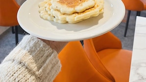 A dining area with white brick walls, orange chairs, and a plate of pancakes on a white plate. - Busselton Motel (West Busselton)