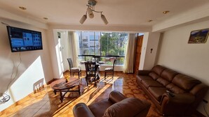 A living room with a brown leather sofa, a wooden coffee table, and a TV mounted on the wall. - Apartment Inti (Cusco)