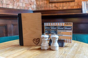 Pizarra de madera con un diseño de corazón, dos saleros y pimenteros, y un menú que enumera opciones para el desayuno.