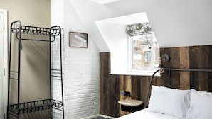 A bedroom with a bunk bed, a small table, a lamp, and a window with a view of buildings.