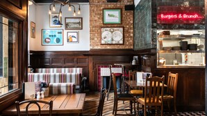 A restaurant interior with wooden furniture, a neon sign for burgers and brunch, and framed pictures on the walls.